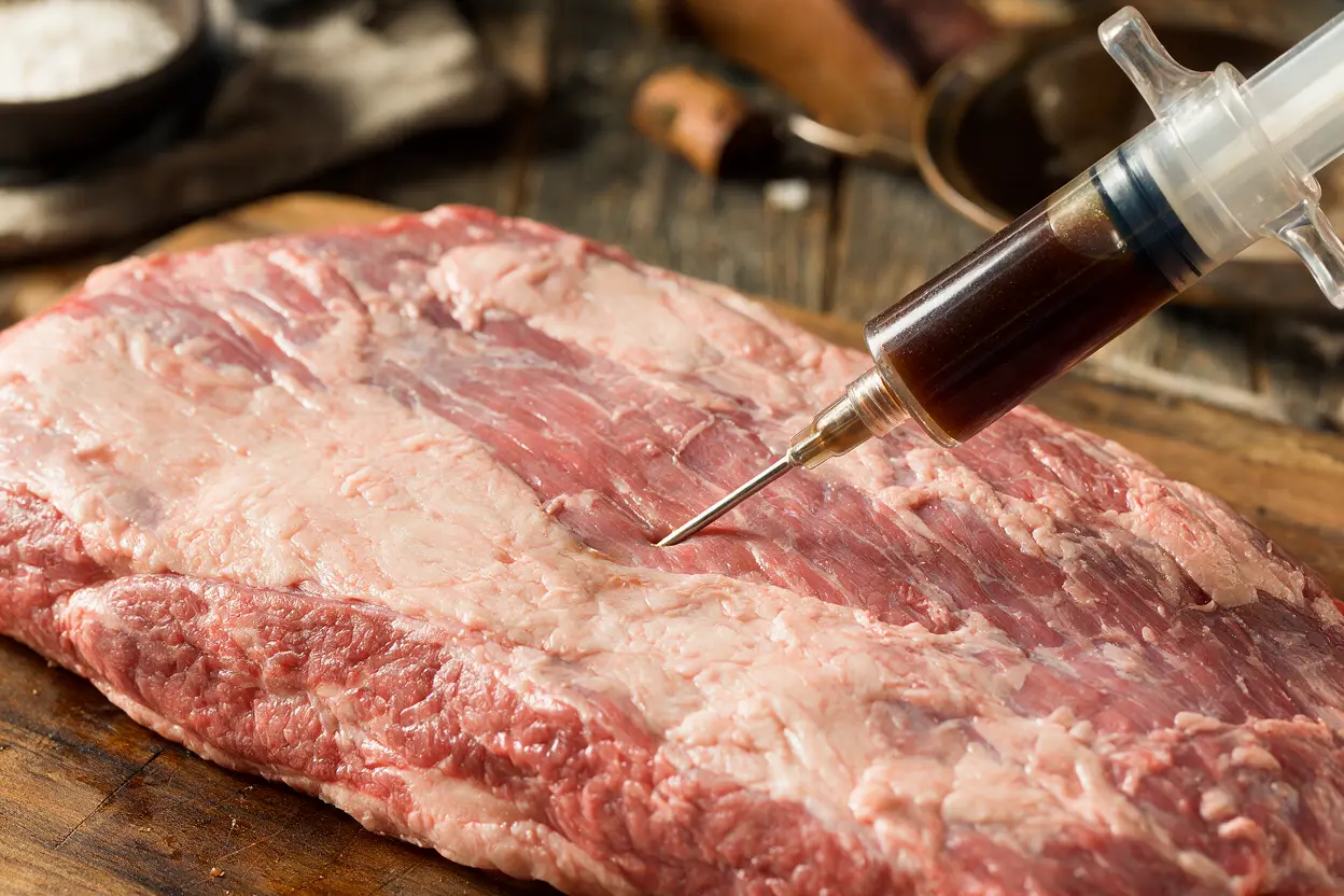 A meat injector inserting beef brisket injection into a raw brisket